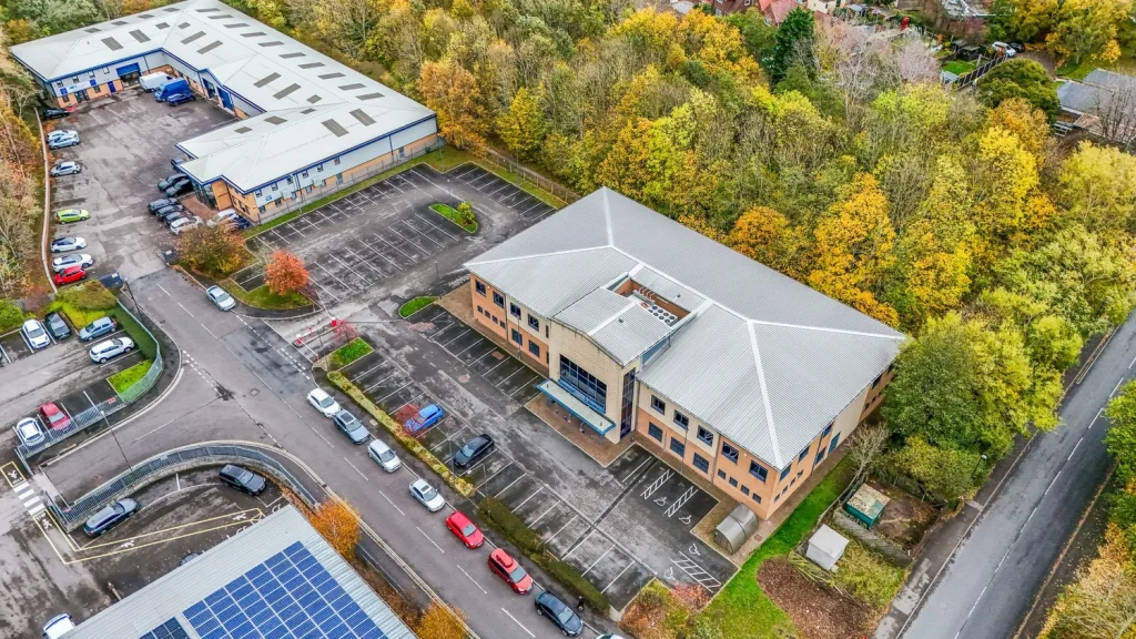 Aerial view of a commercial property with a large building and surrounding parking area, featuring trees in autumn colors.