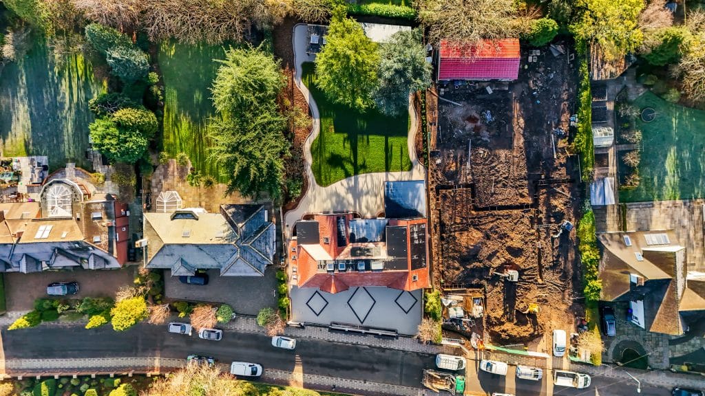 Aerial view of residential properties showing a house with a red roof and a construction site on the right.