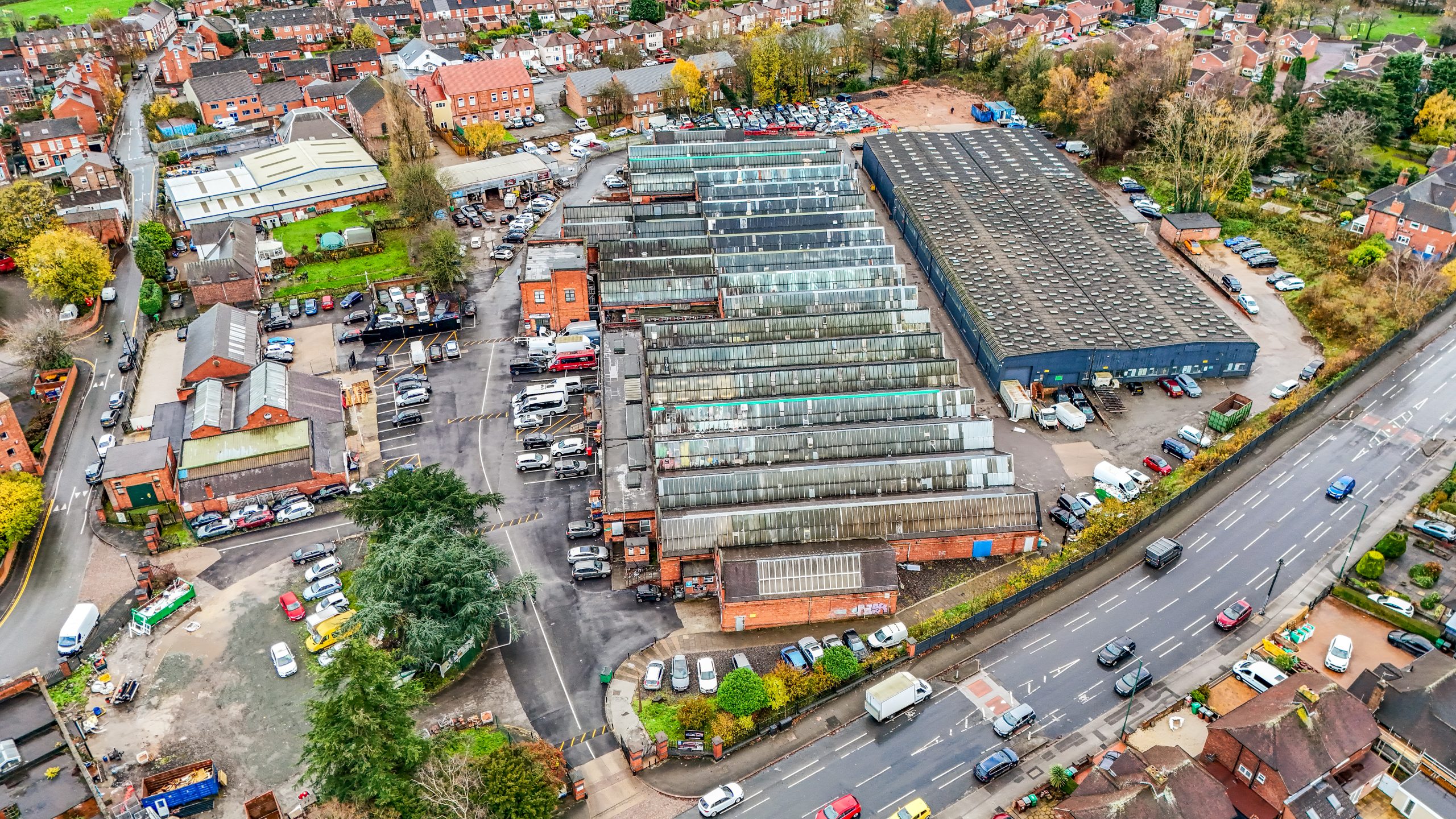 Aerial view of a large industrial complex with multiple buildings and parking areas, surrounded by residential areas and roads.