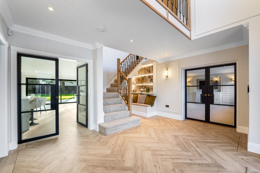 Interior view of a modern home featuring a staircase, glass doors, and herringbone patterned flooring.