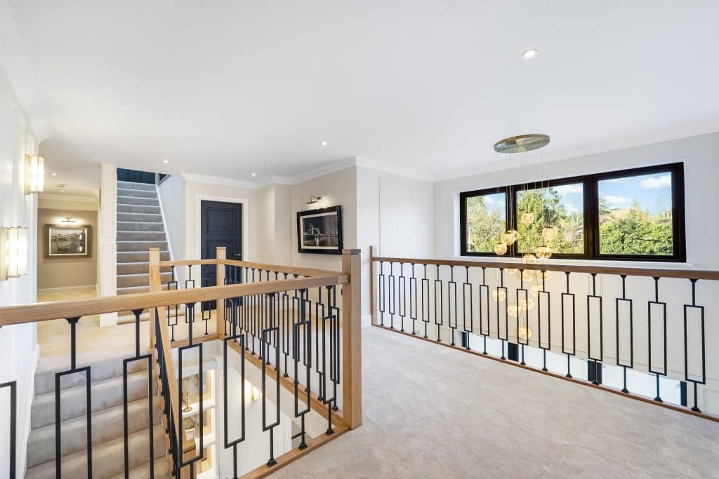 Interior view of a modern staircase landing with wooden railings and a contemporary chandelier.