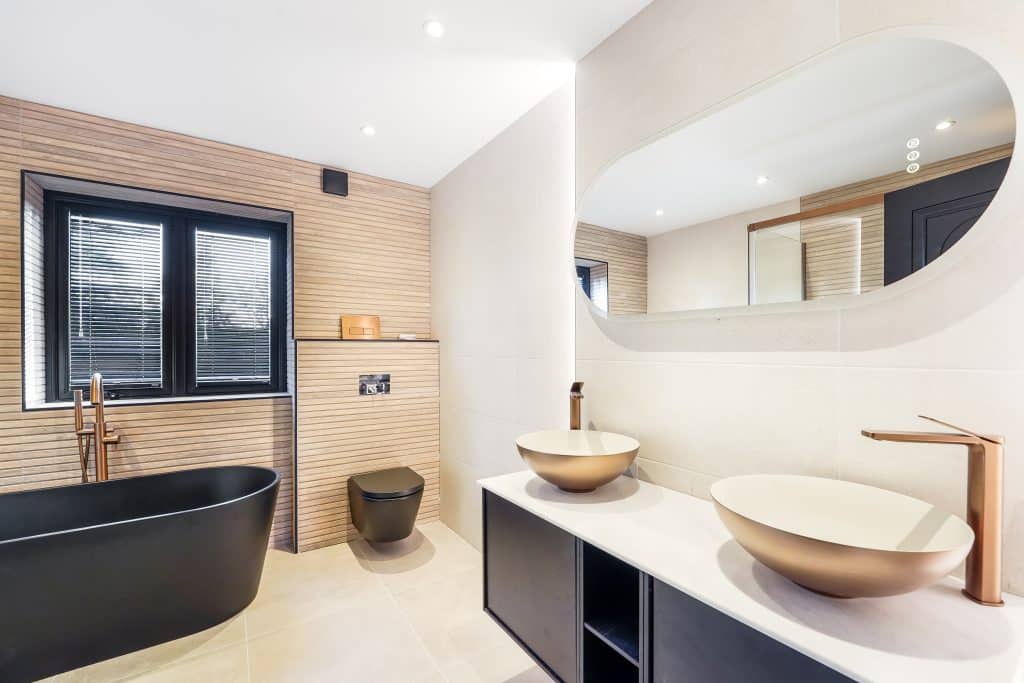 Modern bathroom featuring a black freestanding bathtub, dual round sinks with gold faucets, and a large mirror above a sleek vanity.