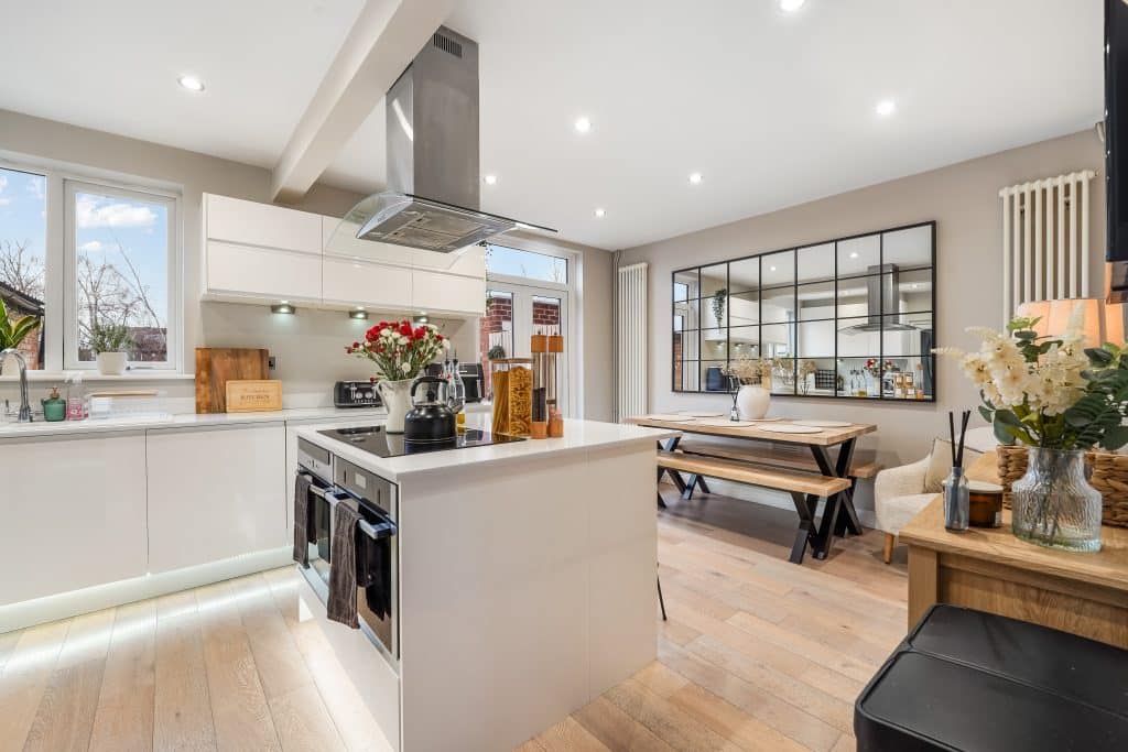 Modern kitchen with white cabinetry, stainless steel appliances, and a wooden dining table. Bright lighting enhances the open space.