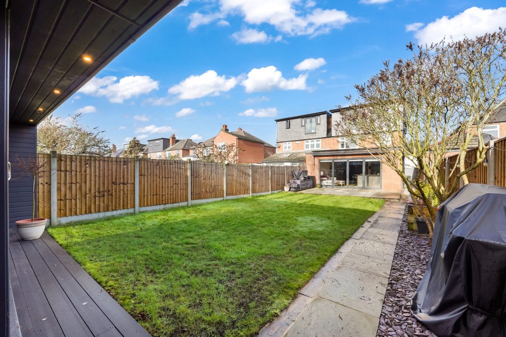 Lawn area with green grass bordered by wooden fencing and a stone pathway leading to a covered patio.