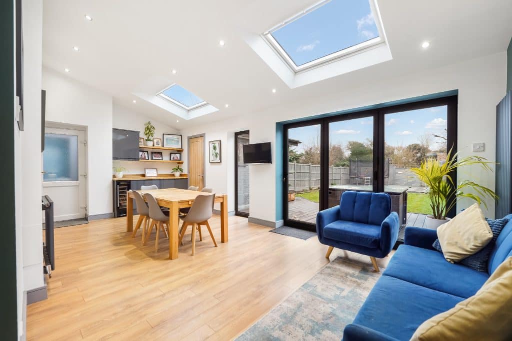 Interior view of a modern living space featuring a dining table, blue sofa, and large windows with skylights.