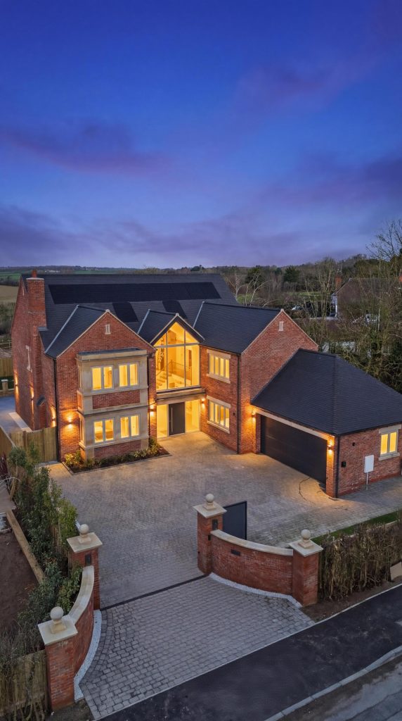 A modern brick house with large windows and illuminated exterior at dusk, showcasing architectural design.